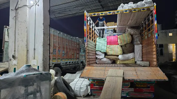 Workers loading bales and cartons into a goods carrier truck for dispatch to Himachal